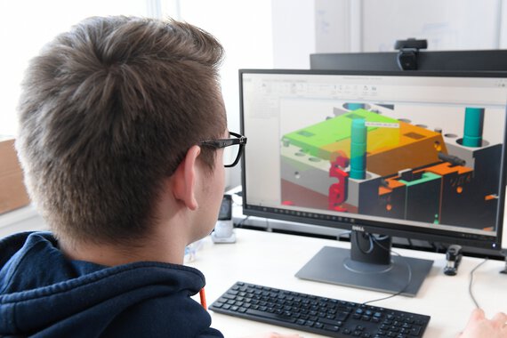 Photo of a Böllhoff apprentice in front of a monitor displaying a design drawing