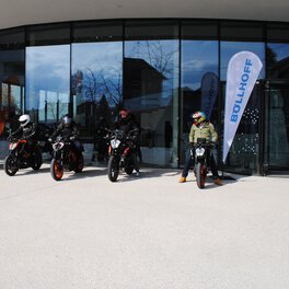 Several motorcyclists stand ready to drive in front of a glass building