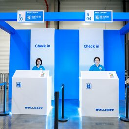 Dos mujeres dan la bienvenida a los visitantes en el mostrador de facturación de la jornada familiar del Grupo Böllhoff en Wuxi, China