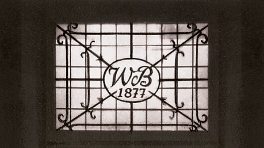 Der Schriftzug "WB 1877" – kurz für Wilhelm Böllhoff 1877 – als Schriftzug aus Metall inmitten eines Fensters