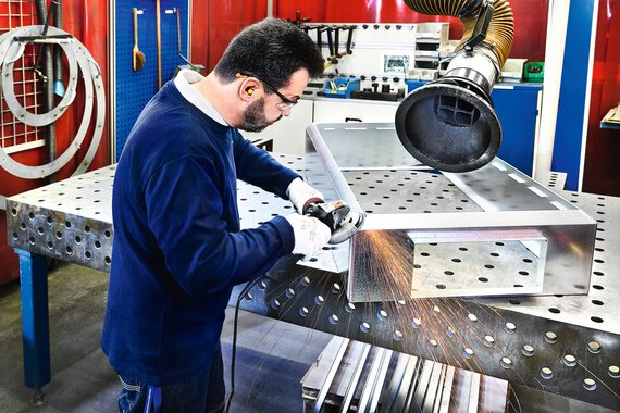 A Trox employee grinds off the edge of a metal container.