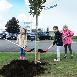 Drei Erstklässlerinnen pflanzen gemeinsam einen Baum auf dem Böllhoff Werksgelände in Bielefeld.