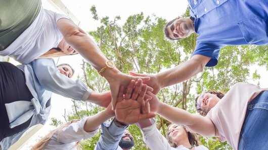 Des collaborateurs du groupe Böllhoff se tiennent en cercle et joignent leurs mains au centre.