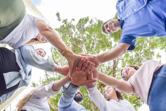 Böllhoff employees stand in a circle and place one hand on top of the other