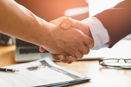 Doi parteneri de afaceri într-un birou își strâng mâna în fața unui birou de lucru