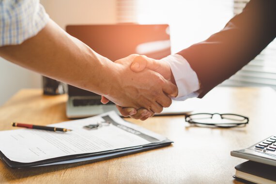 Two business partners in the office shake hands in front of a desk