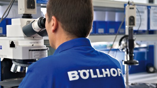 Ein Böllhoff Mitarbeiter prüft die Struktur eines metallischen Werkstoffs mit einem Mikroskop.