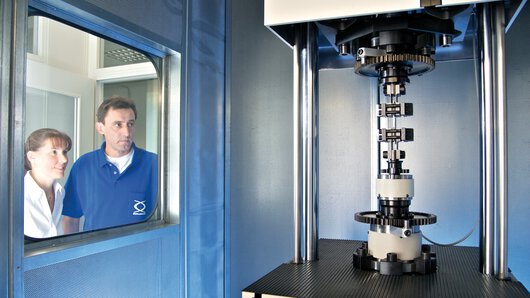 Two employees of the Böllhoff laboratory test the behaviour of a material sample using a vibration testing machine.