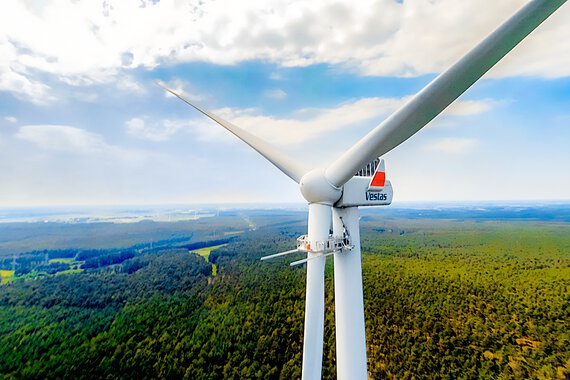 Eine Windkraftanlage in einer Waldlandschaft, mit einer Wartungsbühne von WP Systems am unteren Rotorflügel. In der Wartungsbühne verbaut: Verbindungselemente von Böllhoff.