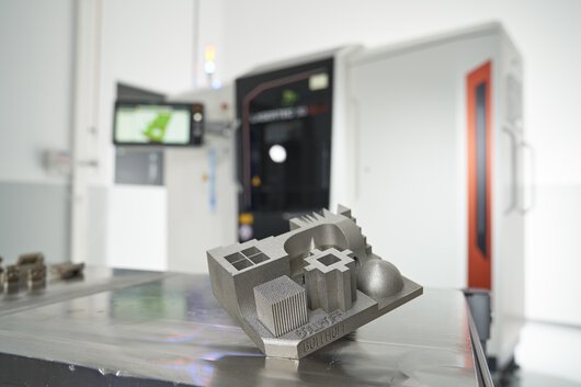 3D-printed component in front of a metal 3D printer at Böllhoff