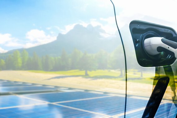 Photo d'une voiture électrique avec une prise de recharge devant un paysage verdoyant et un système photovoltaïque.