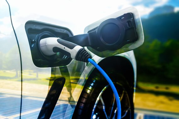 Photo d'une voiture électrique avec une prise de recharge devant un paysage verdoyant et un système photovoltaïque.