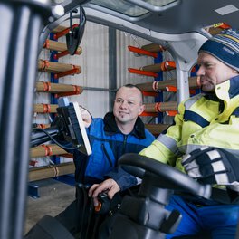 Ein Böllhoff Mitarbeiter sitzt in einem Gabelstapler. Ein weiterer Kollege zeigt auf etwas auf dem Fahrzeugbildschirm