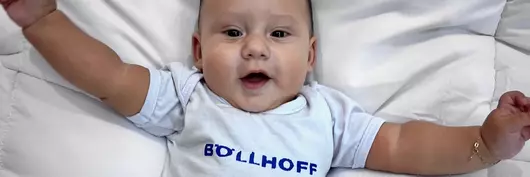 A Brazilian colleague's baby sports a white babygro with Böllhoff logo and looks excitedly at the camera
