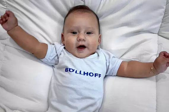 A Brazilian colleague's baby sports a white babygro with Böllhoff logo and looks excitedly at the camera