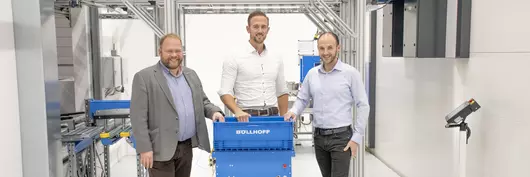 Three employees from Böllhoff assembly manufacturing stand next to an automated guided vehicle system.