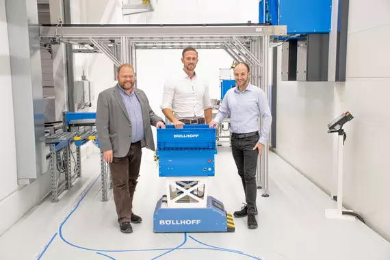 Three employees from Böllhoff assembly manufacturing stand next to an automated guided vehicle system.