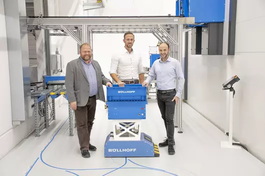 Three employees from Böllhoff assembly manufacturing stand next to an automated guided vehicle system.