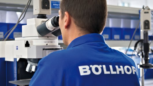 A Böllhoff employee uses a microscope to check the product quality of a fastener