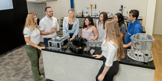 ein Team von Böllhoff Mitarbeitern steht um einen Tisch und hört dem Vortrag eines Kollegen zu