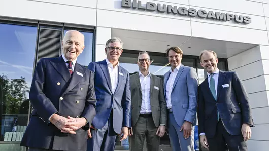 Vor dem Eingang des Bildungscampus Böllhoff stehen 5 Personen aus der Unternehmensleitung und den Bereichen People and Culture und Bildungscampus und lachen in die Kamera. Von links nach rechts: Dr. Wolfgang W. Böllhoff, Wilhelm Alexander Böllhoff, Eike Krull, Frank Nientiedt, Michael Wolfgang Böllhoff.
